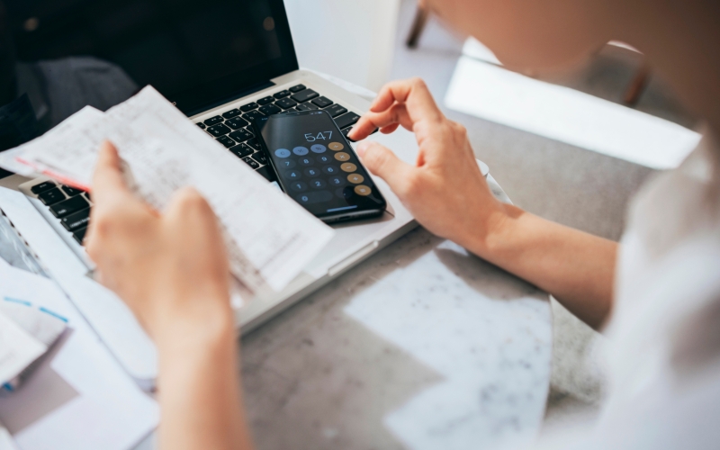 Overhead view of young Asian woman managing personal banking and finance at home. Planning budget and calculating expenses while checking her bills with calculator. Managing taxes and financial bills. Home budgeting. Concept of finance and economy